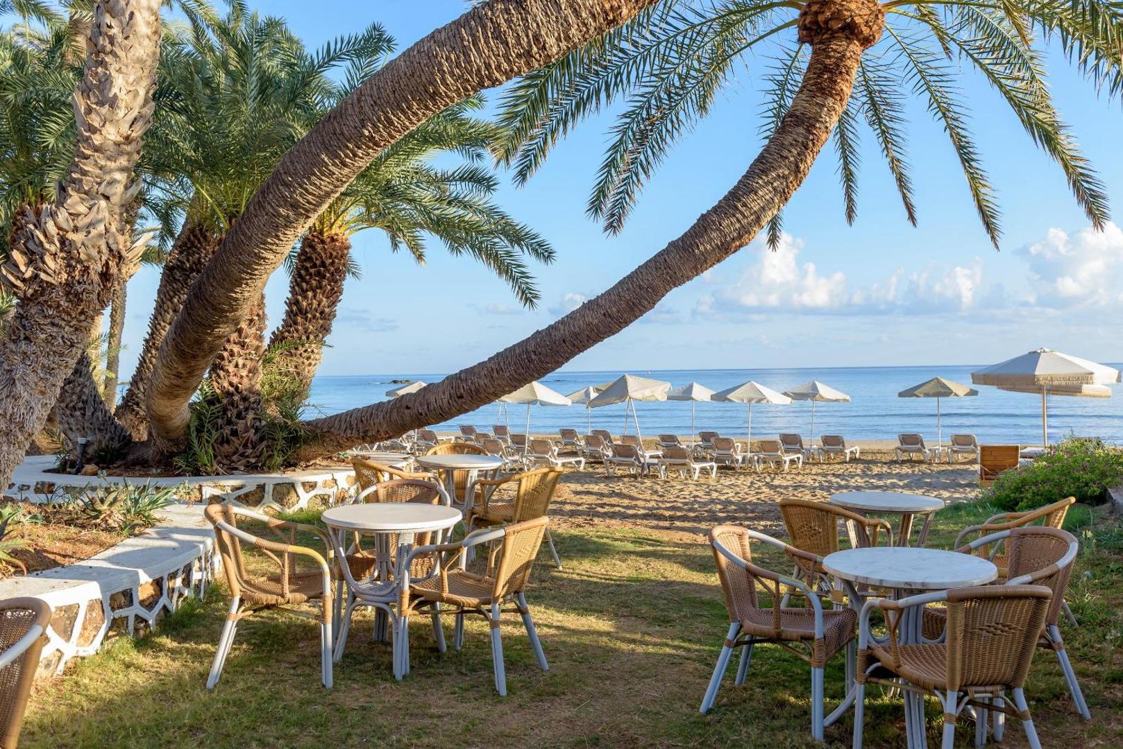 Zeus Palm Beach Hotel āra terase ar galdiņiem palmu pavēnī un skatu uz pludmali un Vidusjūru