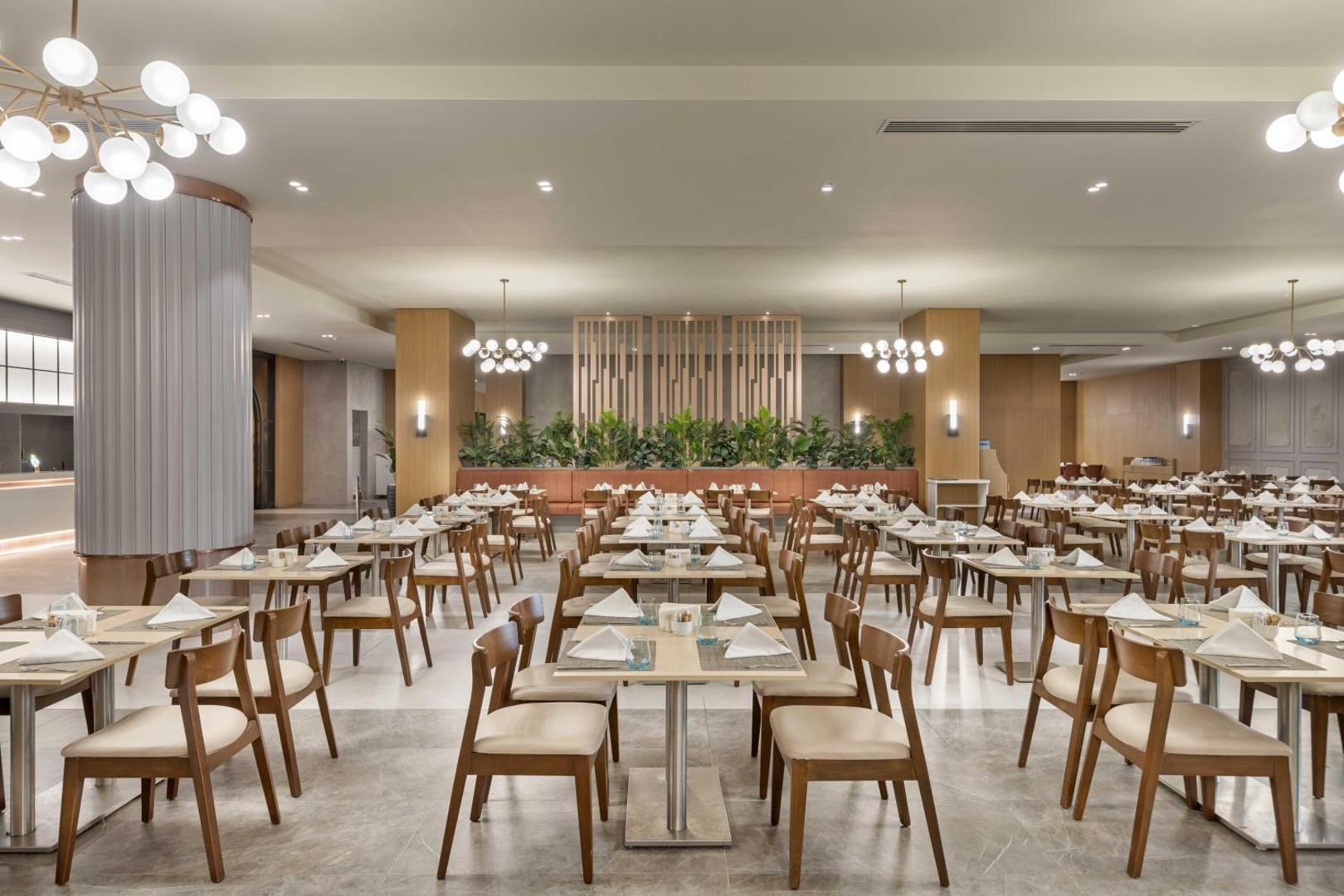 Kirman Hotels Belazur Resort & Spa plašais galvenais restorāns ar modernu interjeru, koka mēbelēm un dekoratīviem augiem Belekā