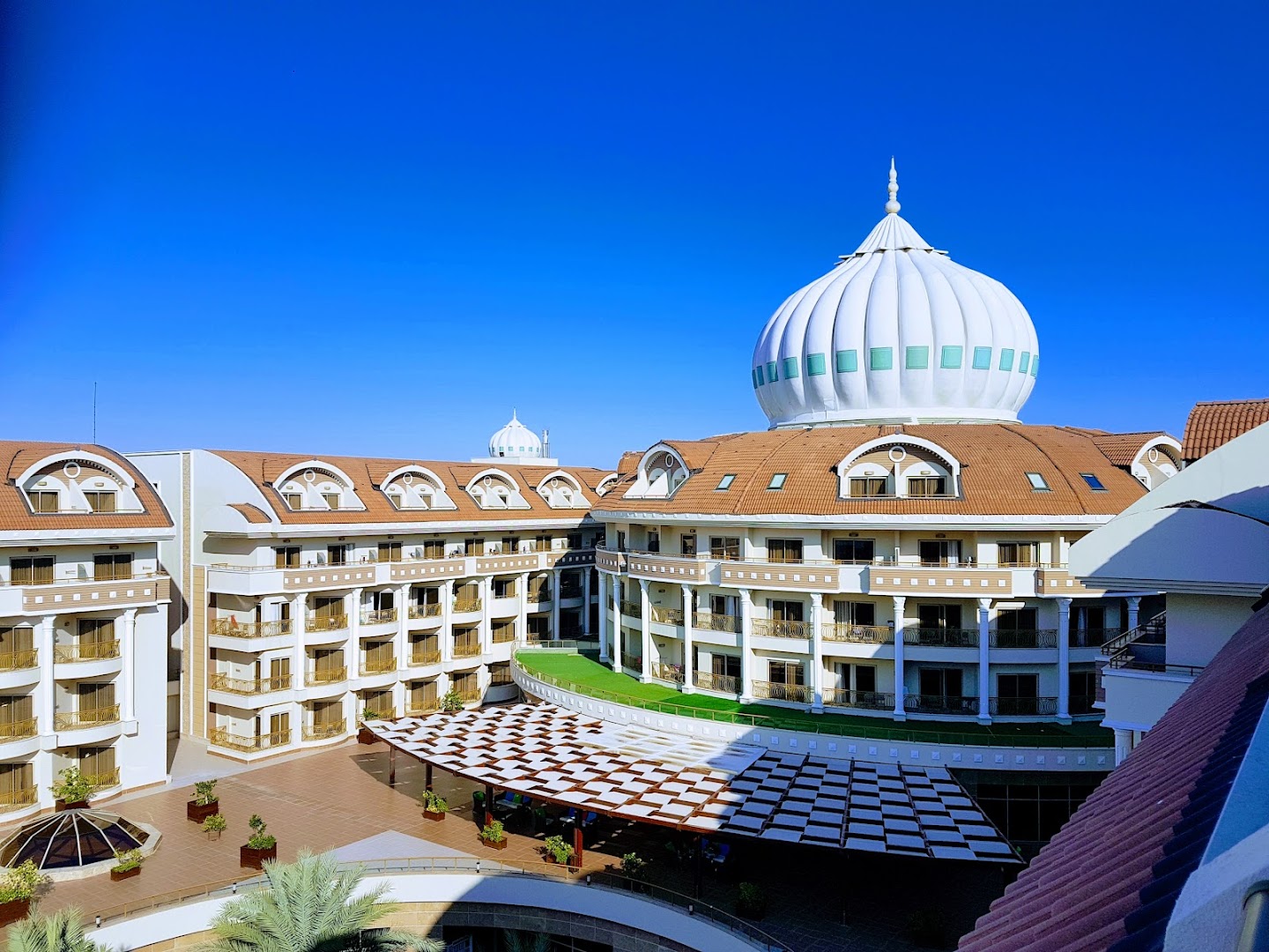 Kirman Belazur Resort & Spa viesnīcas arhitektūra ar raksturīgu baltu kupolu un numuru balkoniem zem skaidrām debesīm Belekā