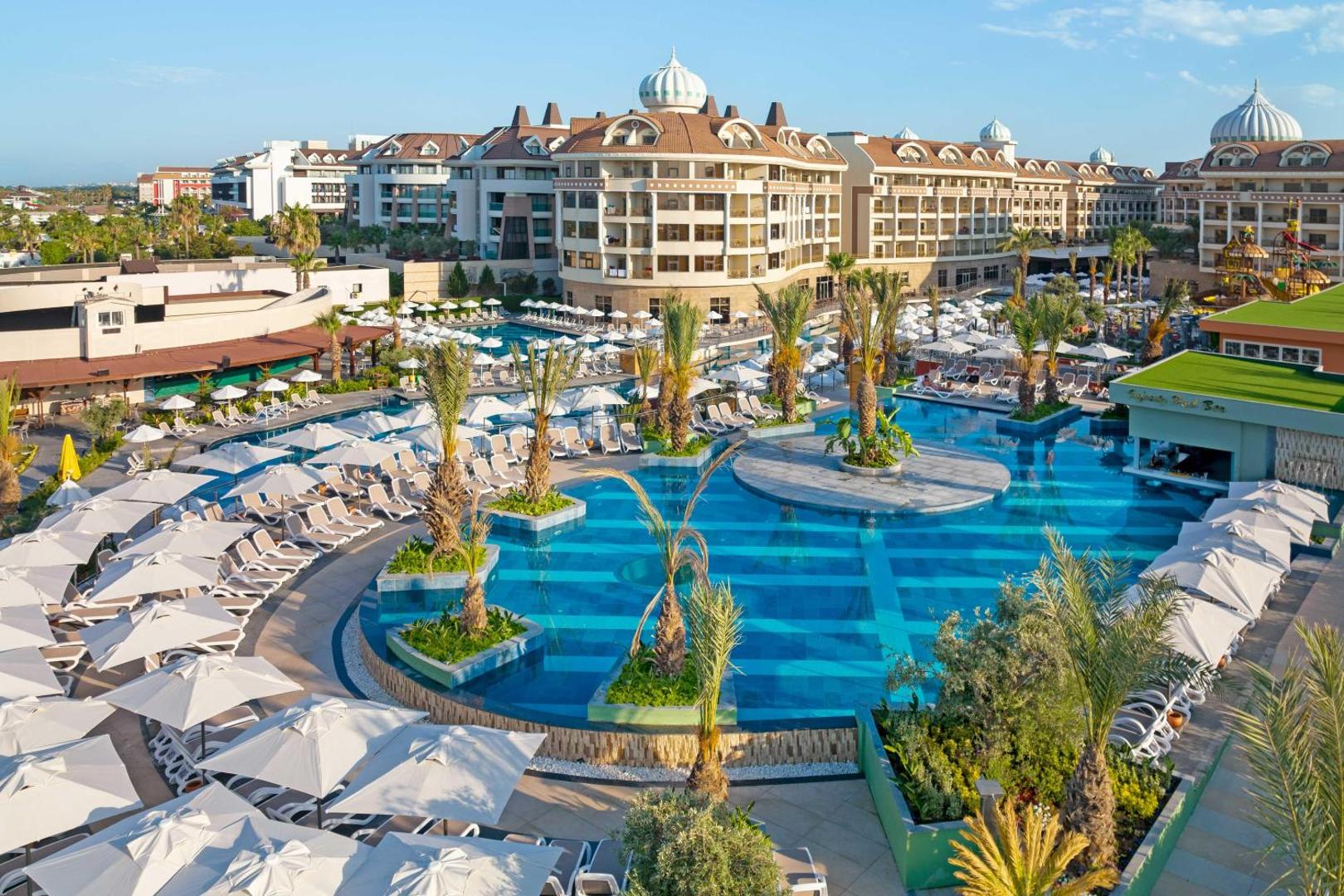 Kirman Hotels Belazur Resort & Spa āra baseinu zona ar saulessargiem, palmām un viesnīcas ēku fonā saulainā dienā Belekā