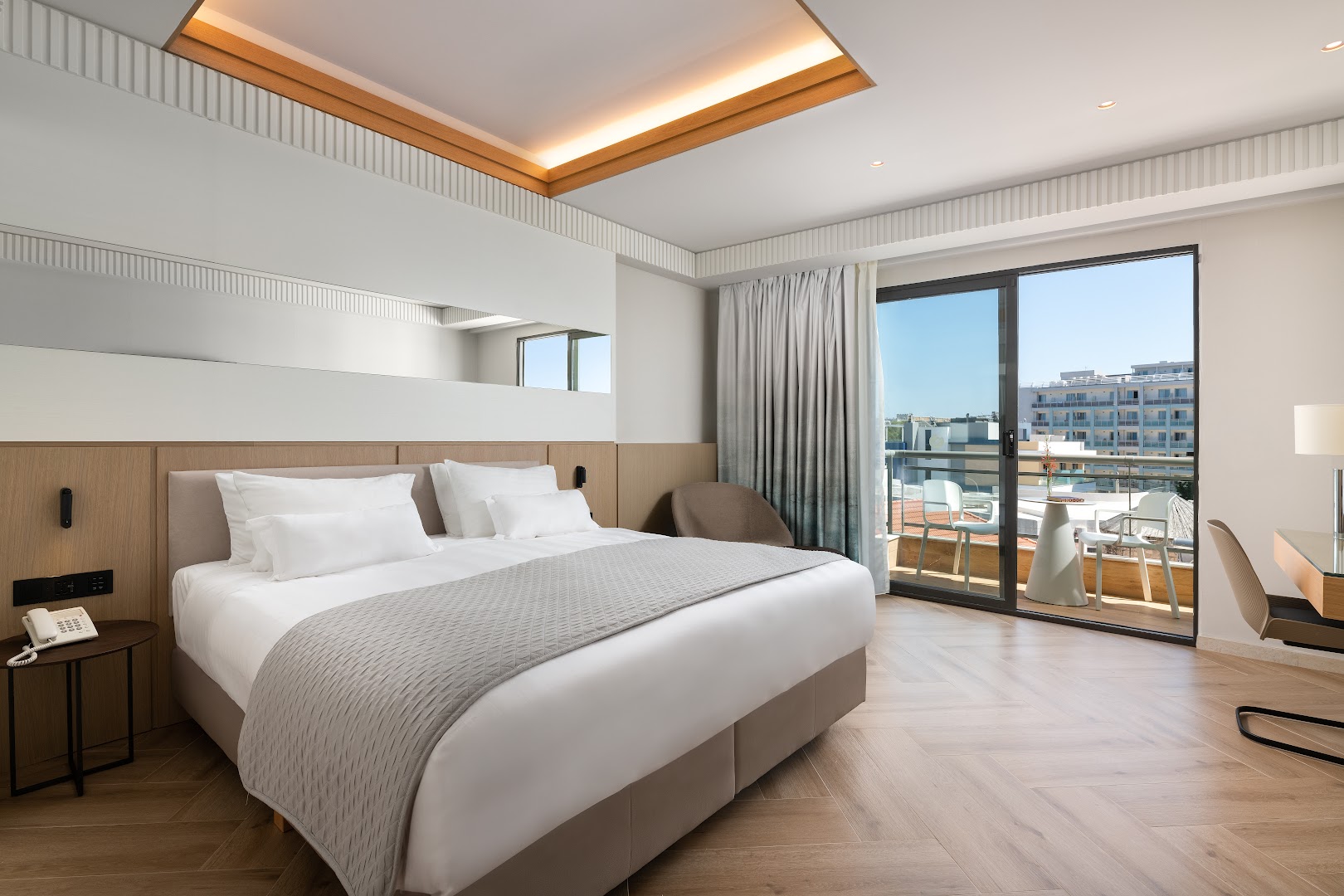 Mediterranean Hotel numurs ar koka grīdas segumu, modernām mēbelēm un balkonu, no kura redzama Rodas pilsētas ainava