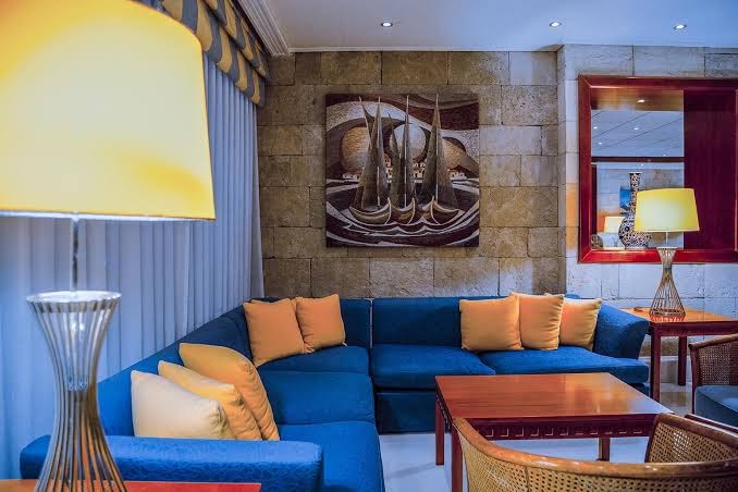 Mediterranean Hotel viesistabas zona ar zilu stūra dīvānu, dekoratīvu gleznu un siltu apgaismojumu mājīgai atpūtai Rodā.