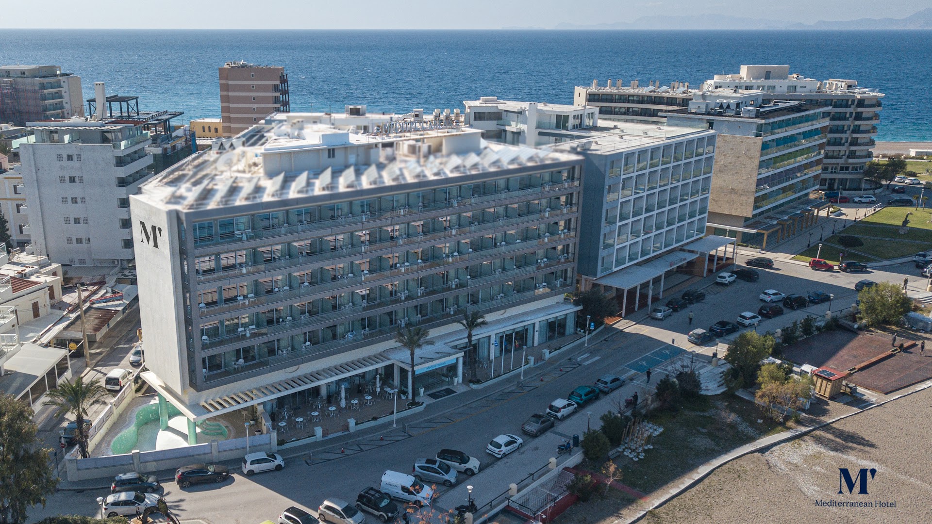 Mediterranean Hotel ēkas skats no putna lidojuma Rodas pilsētā — moderna arhitektūra piekrastē blakus pludmalei un pilsētas infrastruktūrai