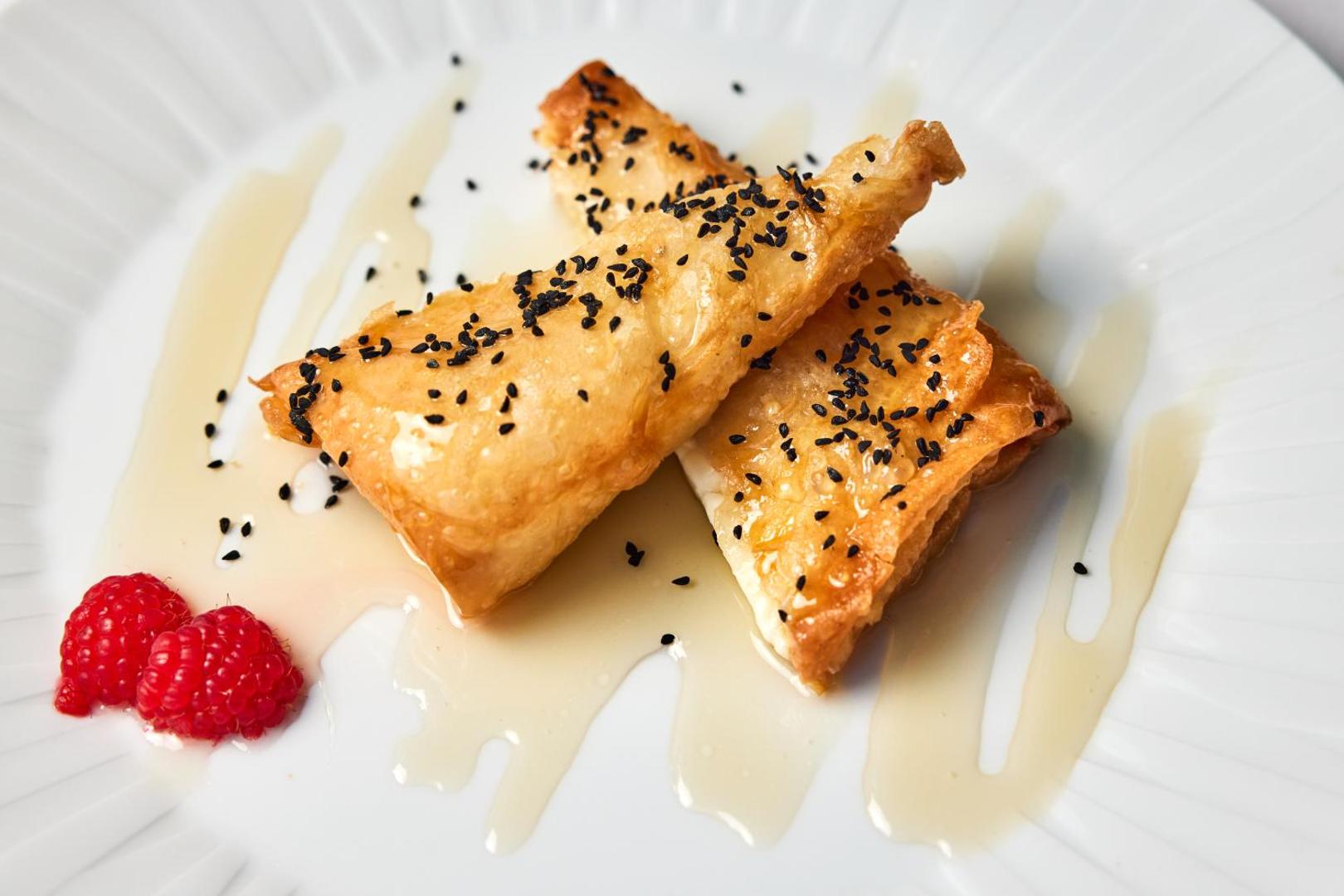 Tradicionāls grieķu deserts ar medu, sezama sēkliņām un avenēm uz balta šķīvja Mediterranean Hotel restorānā Rodas salā.
