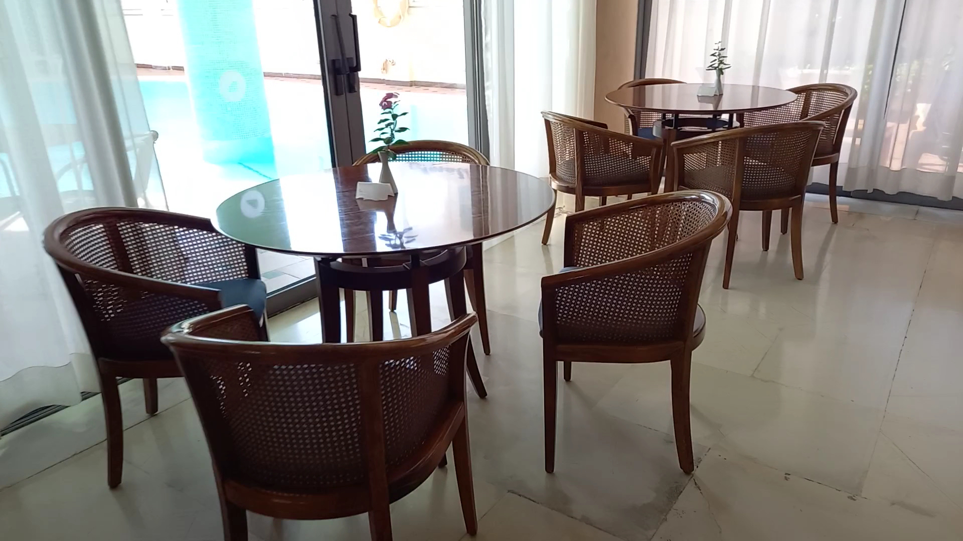 Mediterranean Hotel atpūtas zona ar klasiskiem koka krēsliem un apaļiem galdiem pie stiklota balkona ar skatu uz baseinu Rodā.