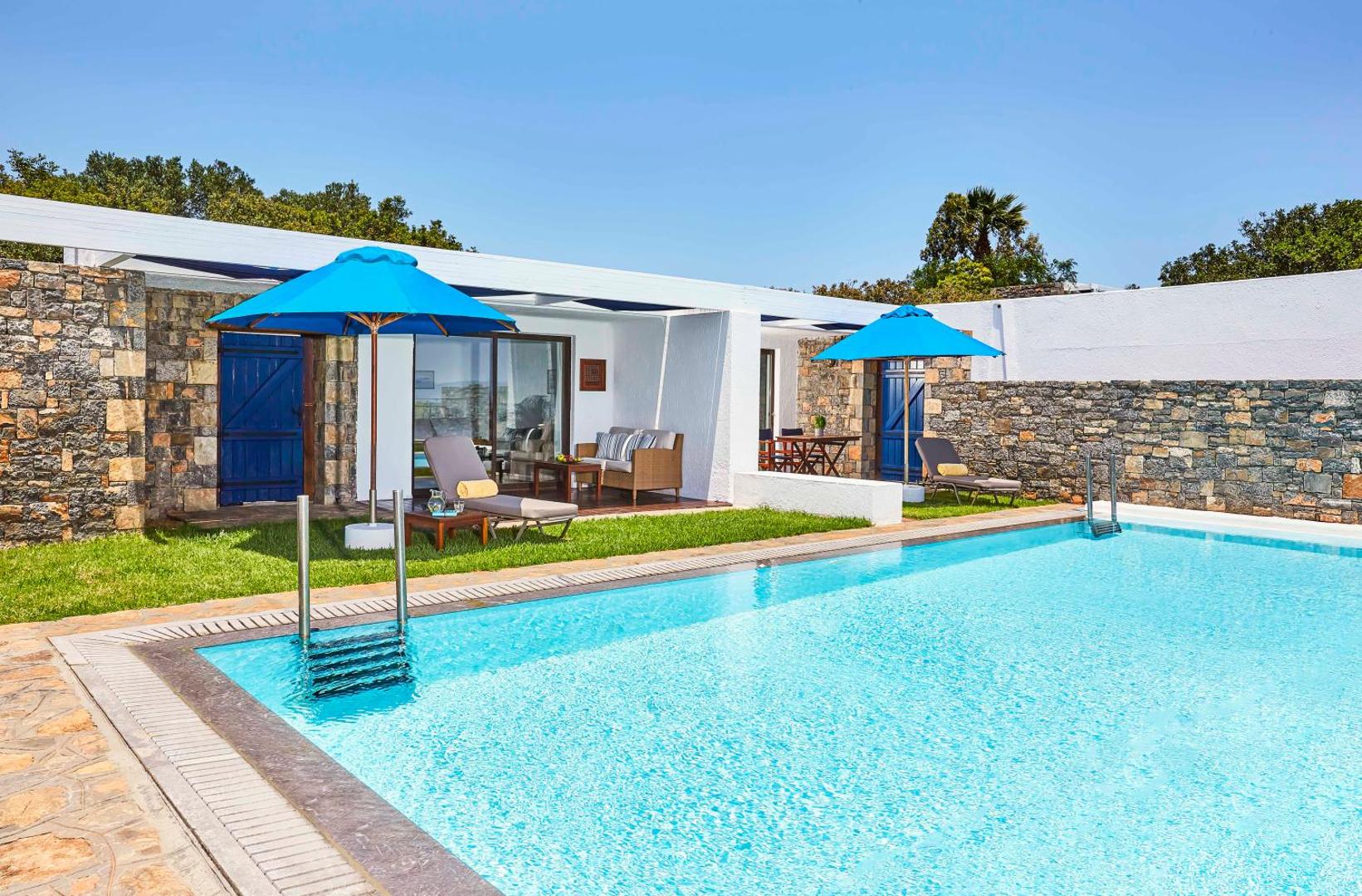 Elounda Bay Palace Hotel bungalo ar tiešu piekļuvi baseinam, akmens mūra sienām un zilu saulessargu terasē Krētas kūrortā