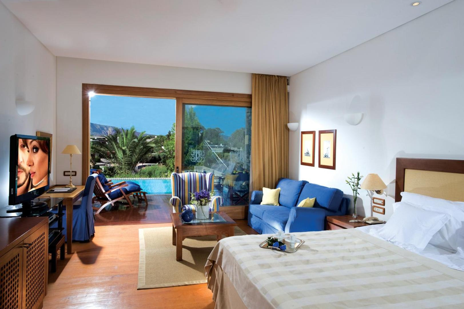 Elounda Bay Palace Hotel numurs ar tiešu piekļuvi baseinam Krētā — koka terase ar atpūtas krēsliem un skatu uz dārzu
