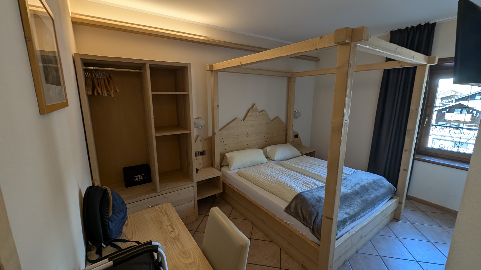 Hotel Lanz gaišs numurs ar koka mēbelēm un baldahīna gultu — Alpu stila interjers ar kalnu motīviem gultas galvgalī