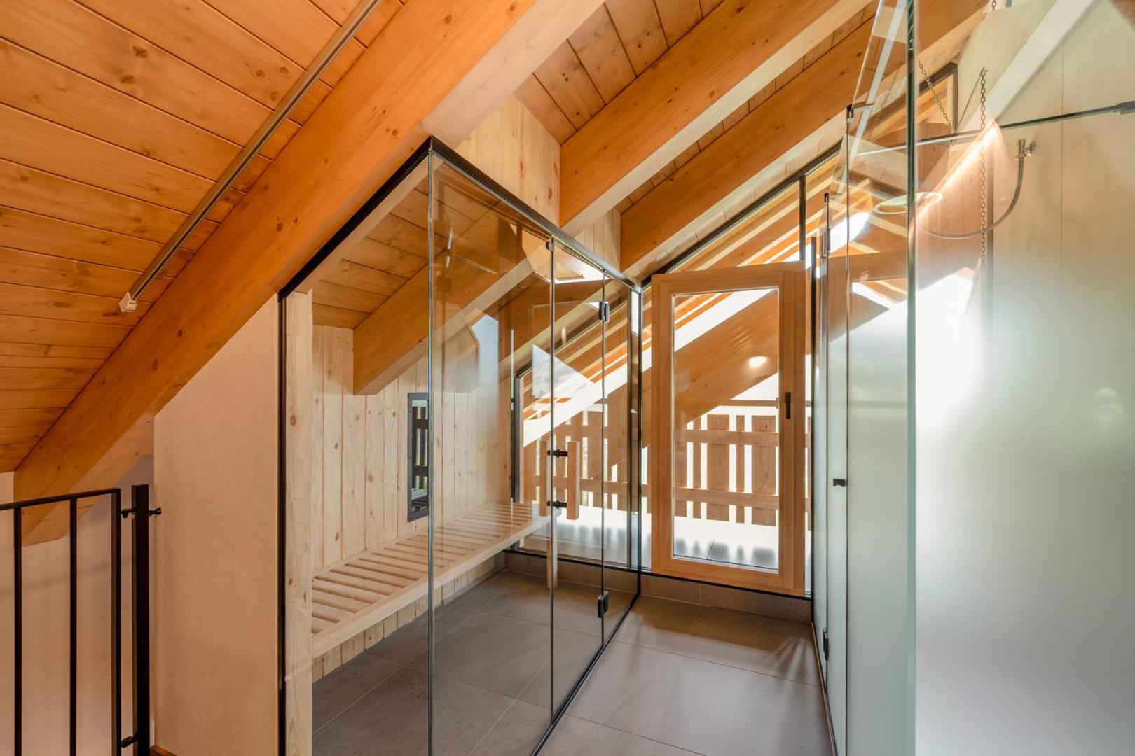 Alpen Resort Bivio moderna sauna ar stikla sienām un koka apdari zem jumta slīpnes, nodrošinot mājīgu atmosfēru