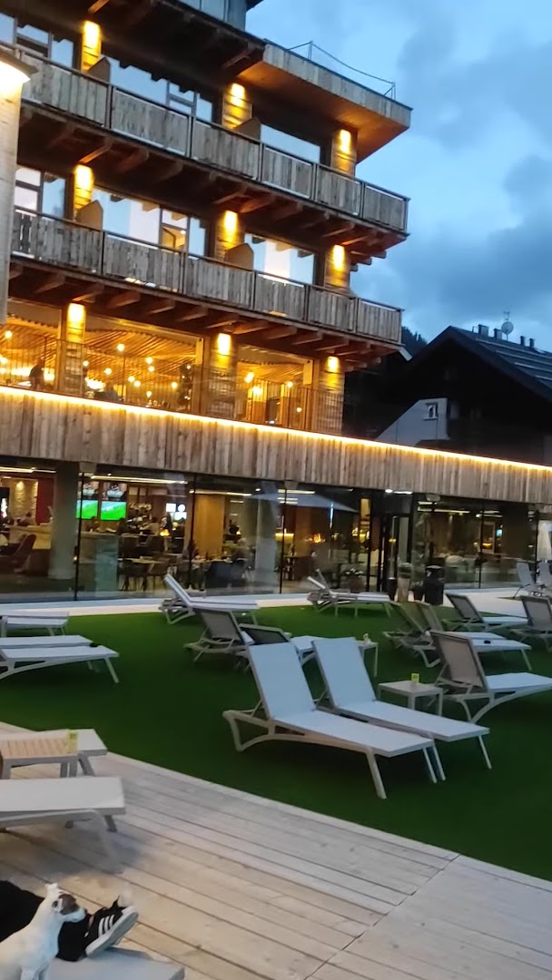 Alpen Resort Bivio vakara apgaismojums terasē ar atpūtas krēsliem — skats uz viesnīcas restorānu un koka konstrukcijām