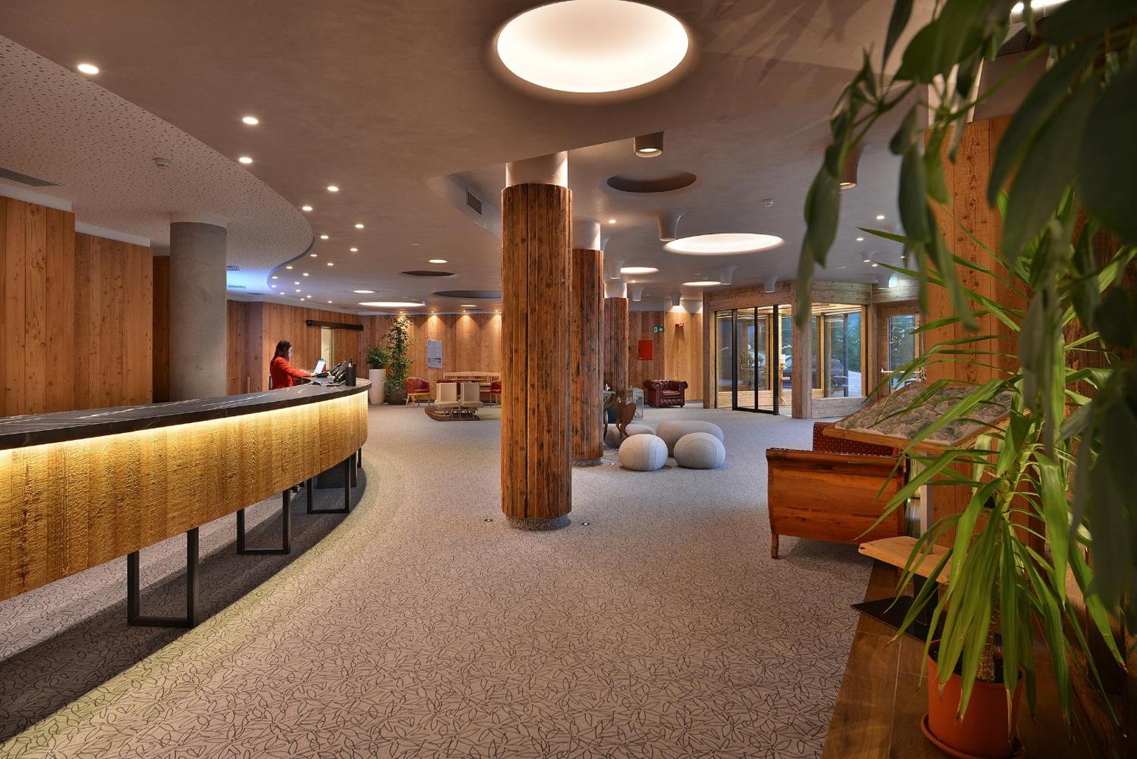 Alpen Resort Bivio plaša lobby zona un recepcija ar koka kolonnām, modernu apgaismojumu un mājīgu interjera dizainu