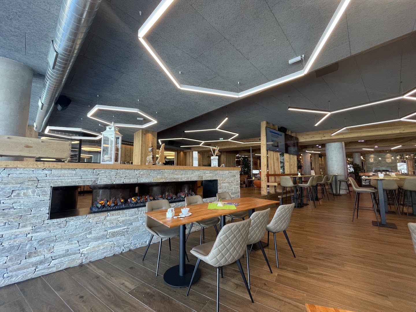 Viesnīcas Alpen Resort Bivio restorāna zona ar kamīnu, koka apdari un elegantiem galdiem, radot mājīgu Alpu atmosfēru Livinjo kūrortā