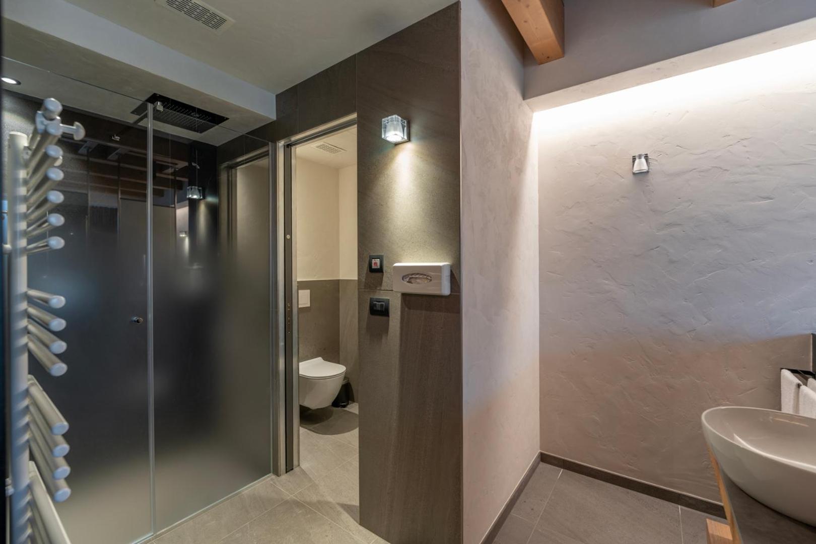 Alpen Resort Bivio numura vannas istaba ar modernu dušas kabīni, tualeti un dizaina izlietni — tumši pelēkas flīzes un silts apgaismojums
