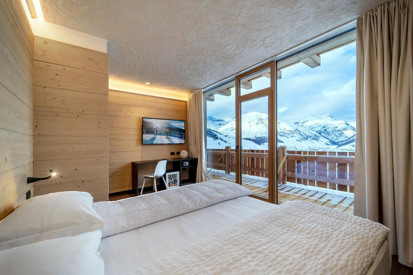 Alpen Resort Bivio numurs ar panorāmas logu uz sniegotajiem kalniem — gaišs koka interjers un balkons Livinjo Alpos