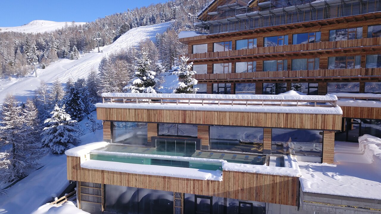Alpen Resort Bivio viesnīcas koka fasāde un āra baseina zona ziemā, blakus slēpošanas trasei un apsnigušām priedēm