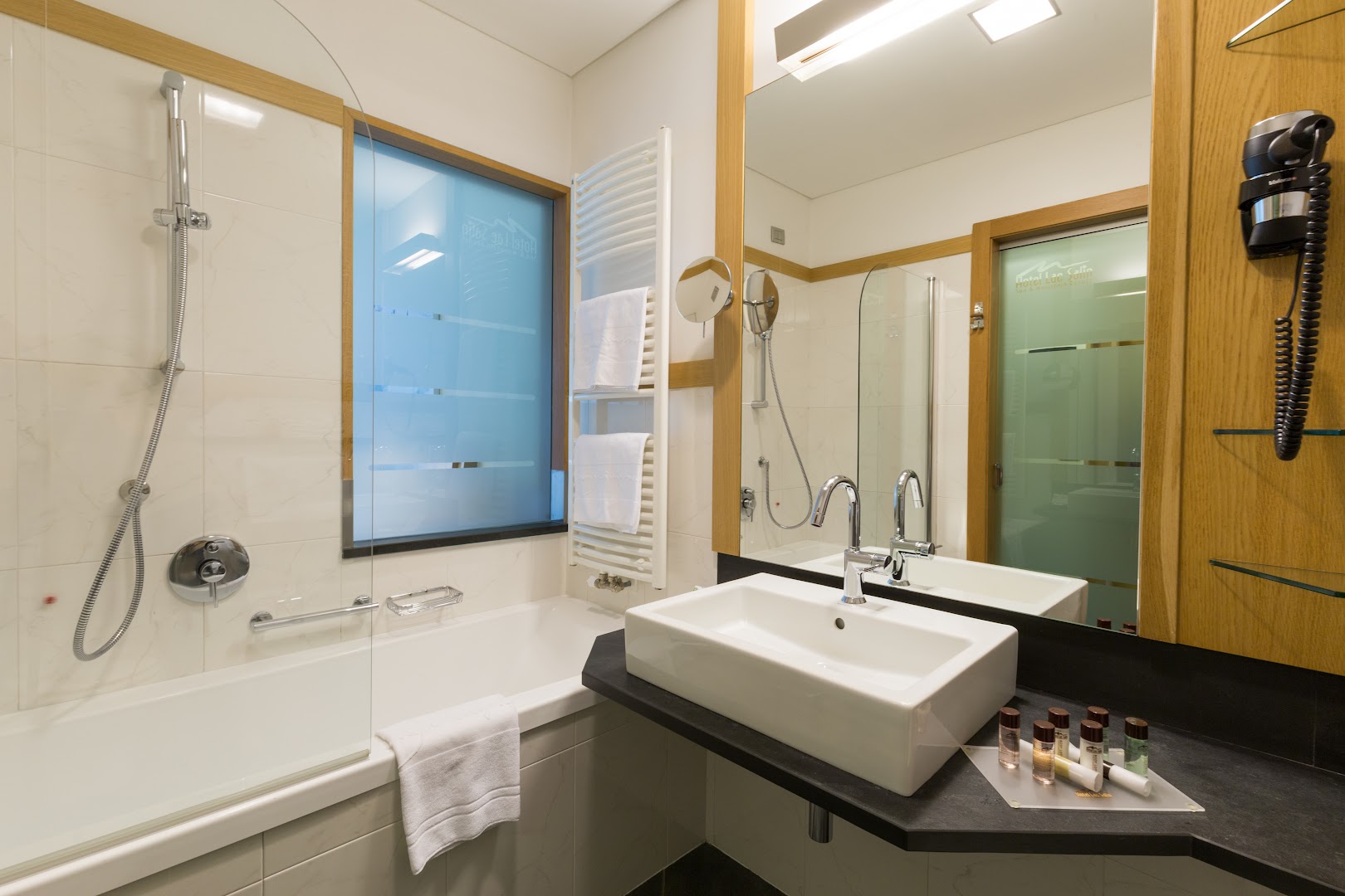 Lac Salin Spa & Mountain Resort numura vannas istaba ar vannu, modernu izlietni un gaišu flīžu apdari kalnu kūrortā Itālijā