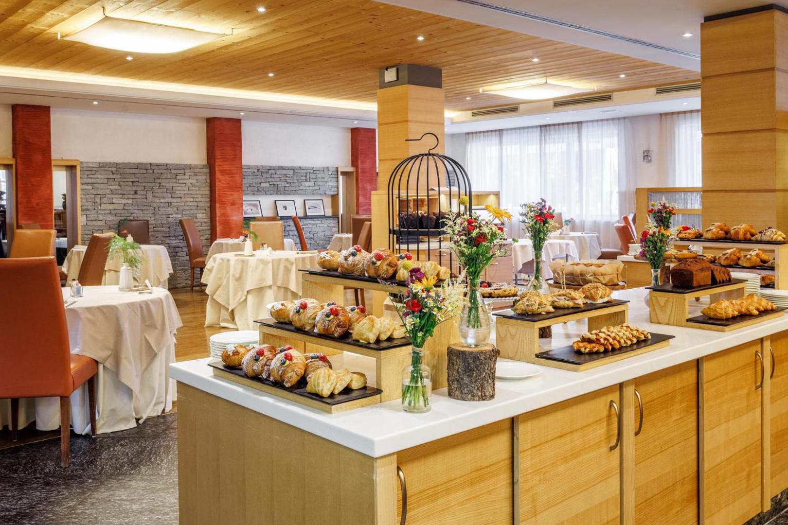 Lac Salin Spa & Mountain Resort brokastu bufete ar svaigām smalkmaizītēm, kruasāniem un ziedu dekorācijām gaišā restorāna zālē