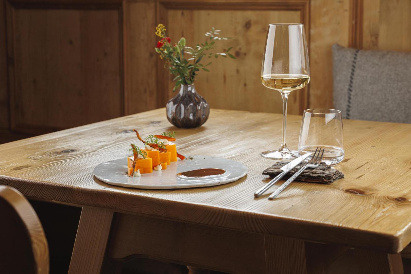 Gourmet vakariņas Lac Salin Spa & Mountain Resort restorānā — eleganti pasniegts ēdiens uz koka galda ar vīna glāzi Alpu stilā