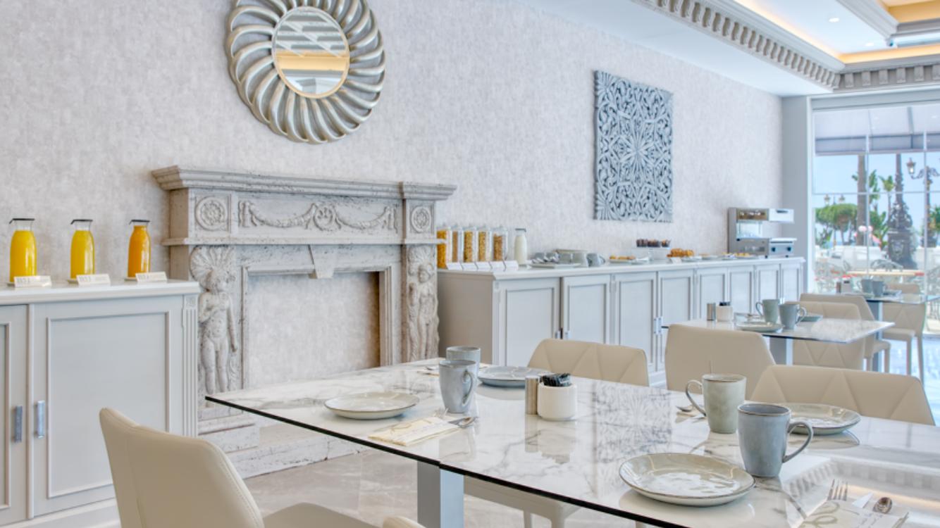 Hotel Boutique B51 brokastu zāle ar marmora galdiem, dekoratīvu kamīnu un bufetes zonu ar svaigām sulām un uzkodām.