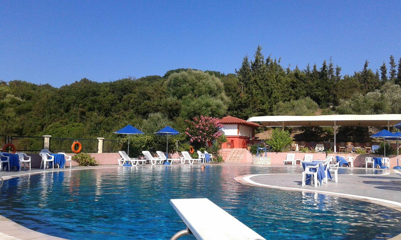 Brati Arkoudi Hotel baseins ar tramplīnu, galdiņiem un bāru fonā, ko ieskauj kalni un mežs.