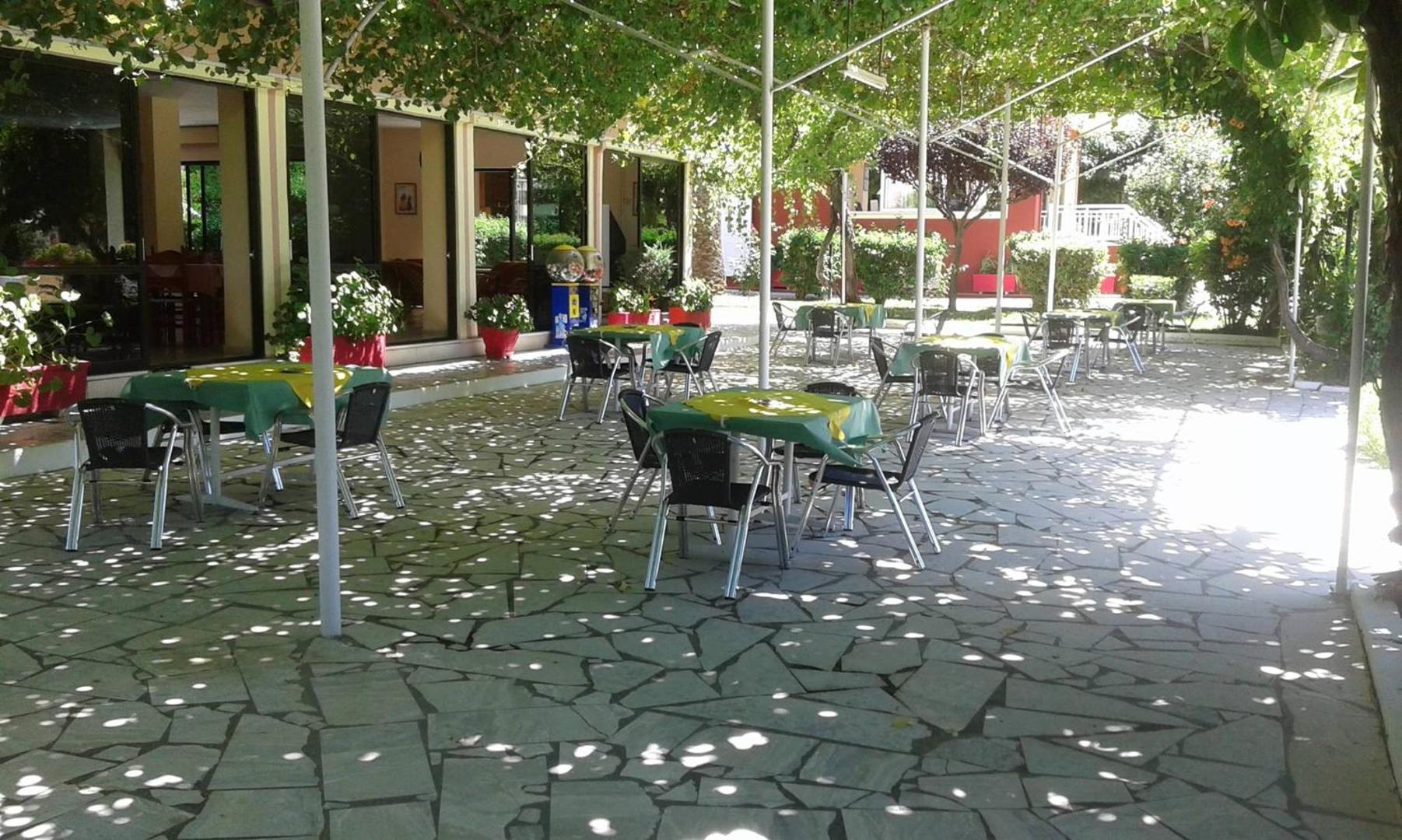 Brati Arkoudi Hotel āra terase koku ēnā ar galdiņiem un tradicionālu akmens flīžu klājumu