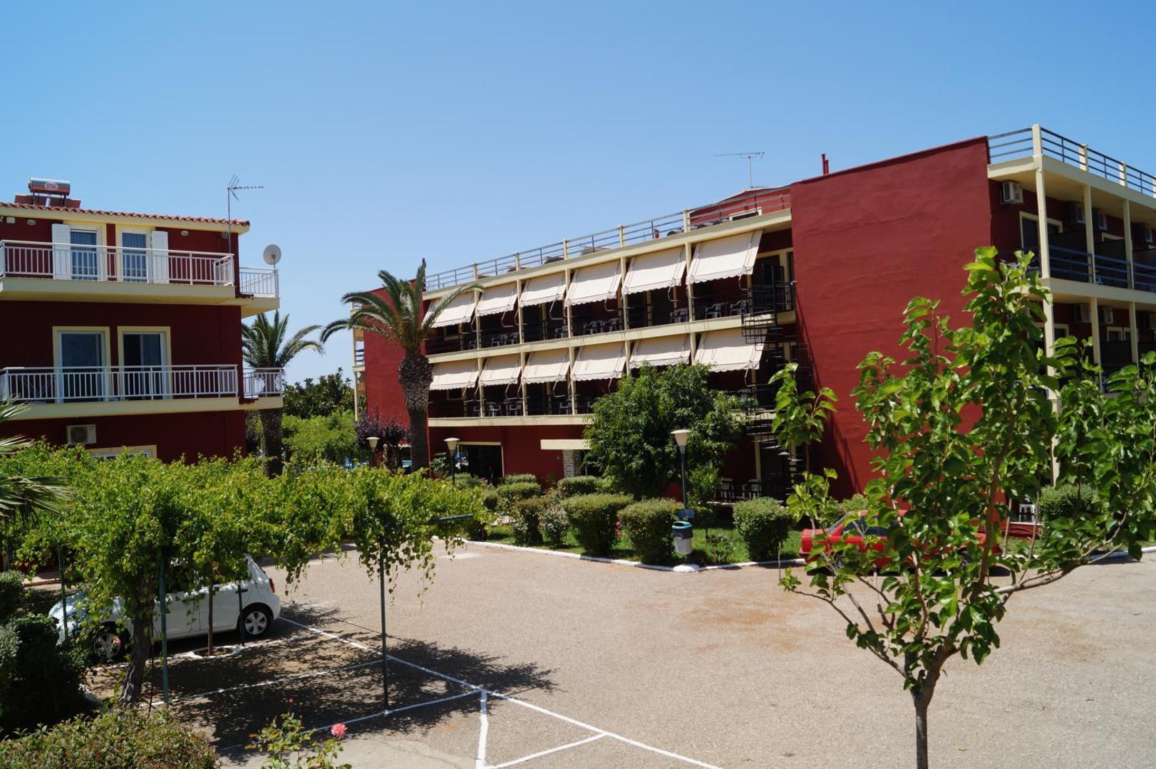 Brati Arkoudi Hotel ēkas fasāde Arkoudi ciematā, Peloponēsā — skats uz numuru balkoniem, palmu dārzu un viesnīcas pagalmu