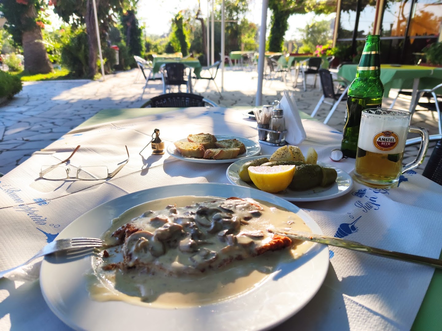 Brati Arkoudi Hotel restorāna āra terase ar klātu galdu — grieķu virtuve, uzkodas un atvēsinoši dzērieni saulrietā