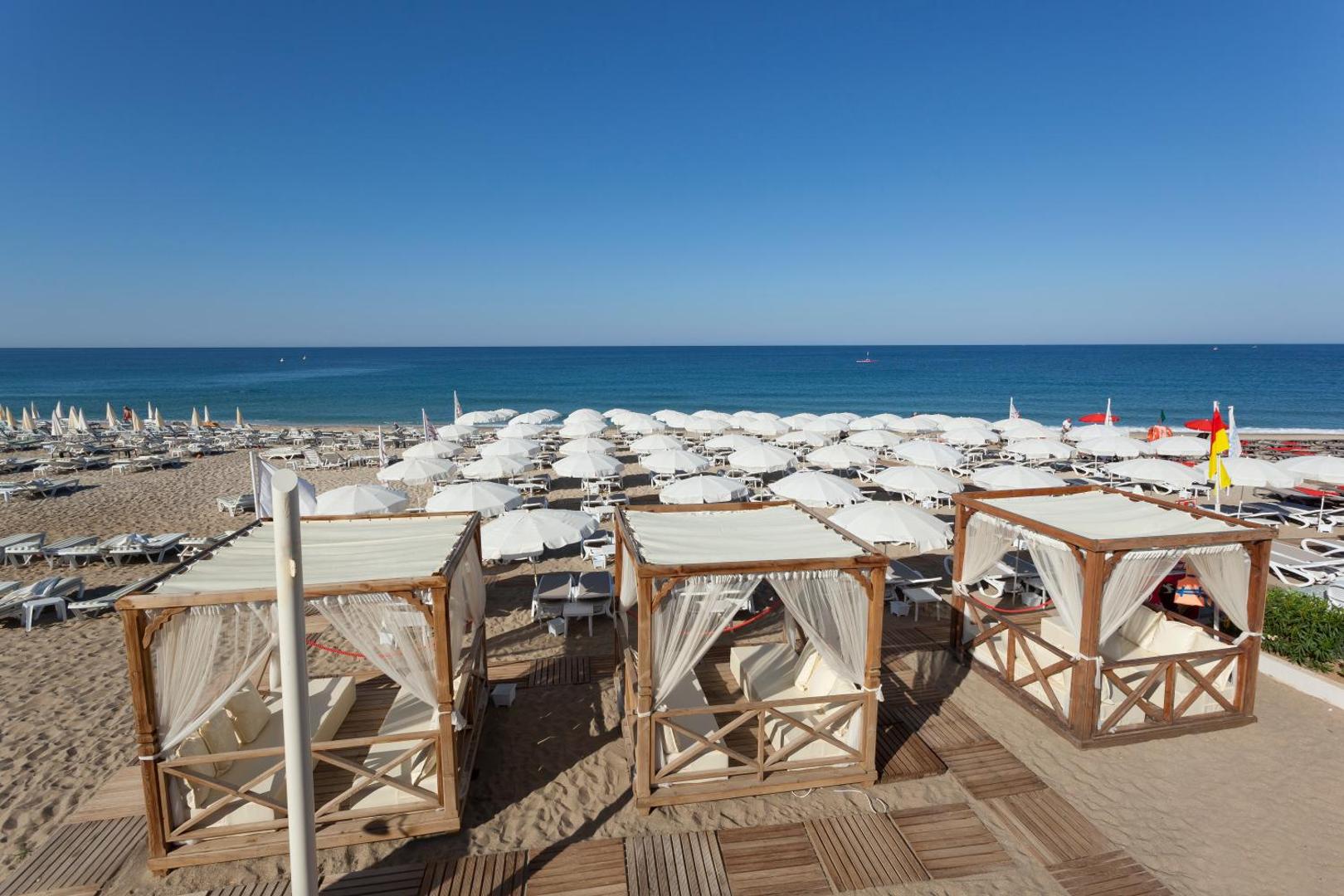 Xperia Saray Beach pludmales zona ar baltiem saulessargiem un privātām atpūtas nojumēm jeb bungalo Alanjas piekrastē pie zilas jūras