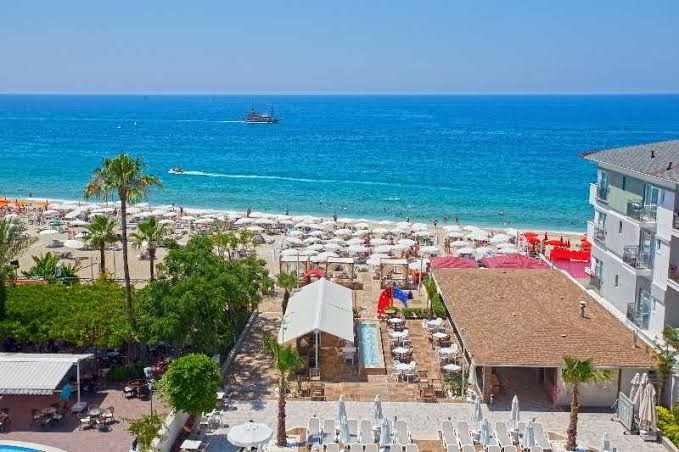 Xperia Saray Beach pludmales zona Alānijā — skats no augšas uz zilo jūru, saulessargiem un viesnīcas āra terasi piekrastē