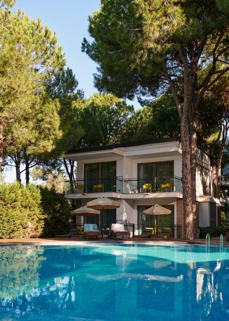 Divstāvu bungalo ēka Voyage Belek Golf & Spa teritorijā, ko ieskauj lieli koki un baseina zona