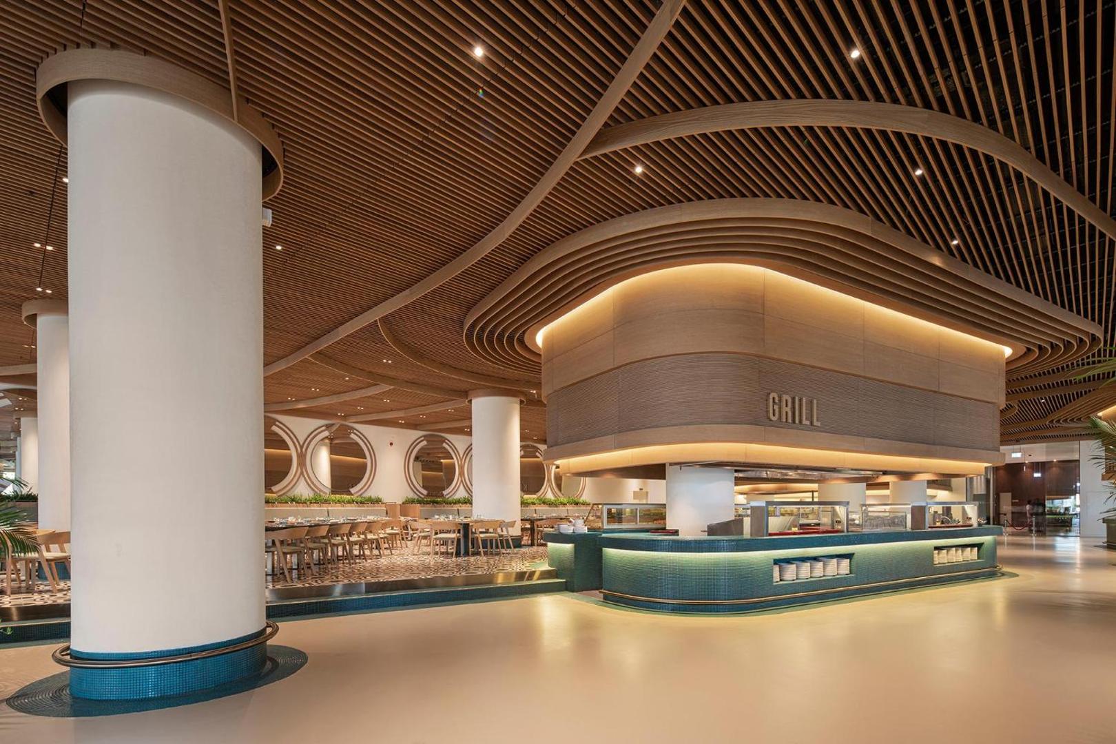 Voyage Belek Golf & Spa galvenā restorāna grila zona ar modernu koka griestu dizainu un apgaismojumu