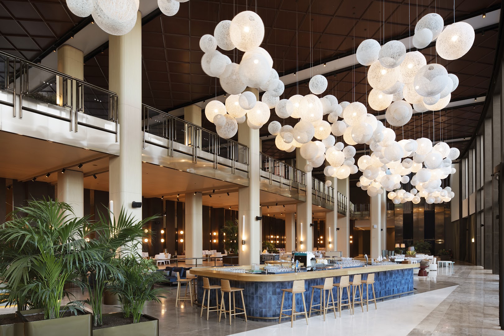 Voyage Belek Golf & Spa viesnīcas lobby bārs ar modernām gaismas instalācijām, zilu flīžu apdari un augstiem griestiem Belekā, Turcijā