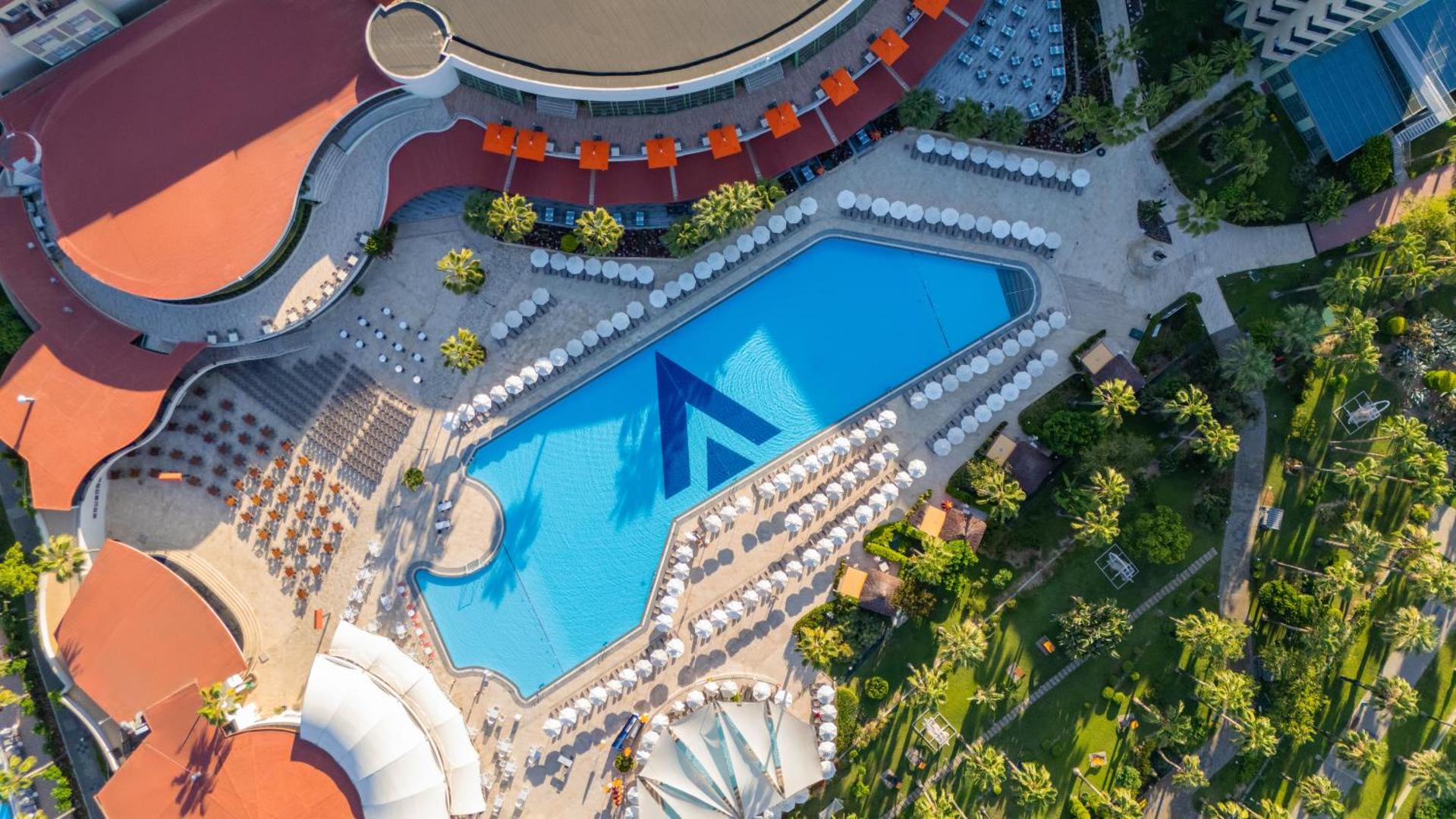 Aerofoto skats uz VONRESORT Golden Coast galveno baseinu, apkārtējo terasi ar saulessargiem un labiekārtotu zaļo dārzu