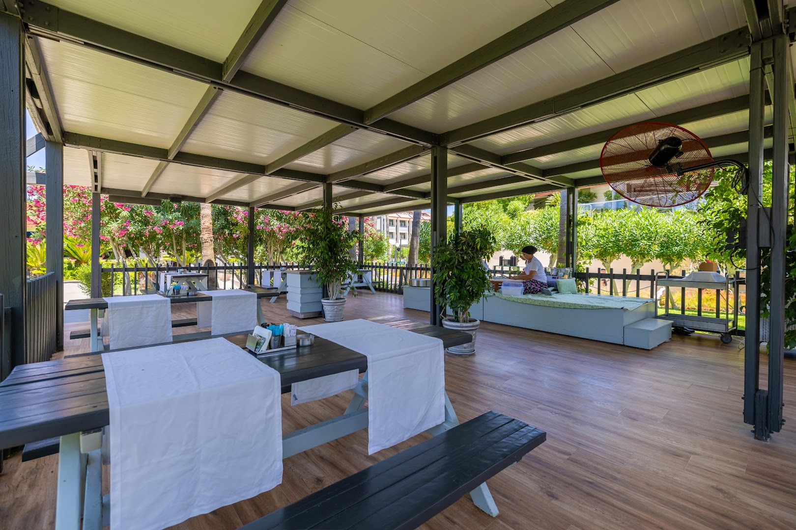 Von Resort Golden Coast āra terases restorāns ar koka galdiem un soliem zem nojumes dārza ielenkumā