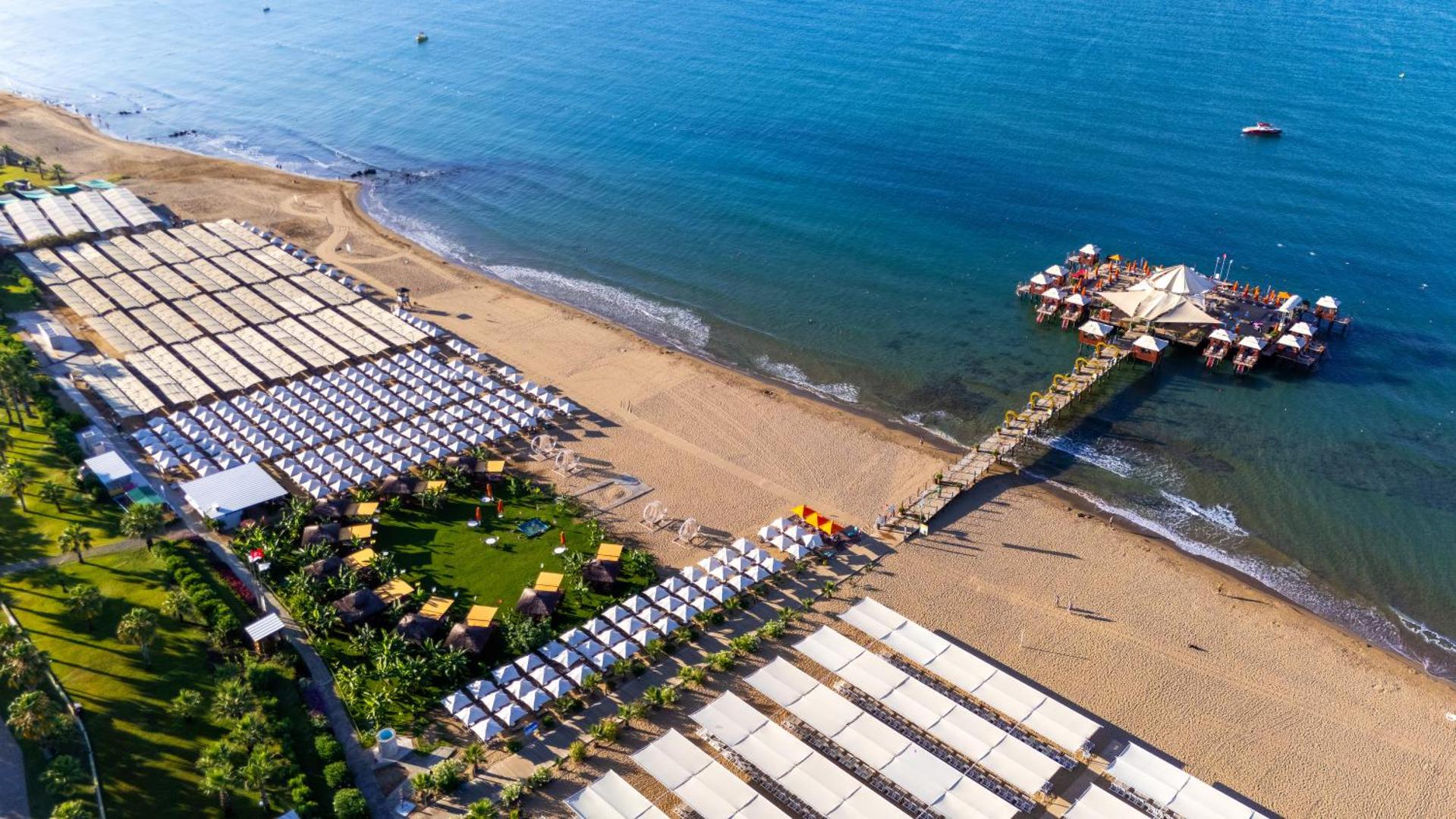 Von Resort Golden Coast pludmales piestātne no putna lidojuma ar saulessargiem, gultām un atpūtas namiņiem virs ūdens Sidē.