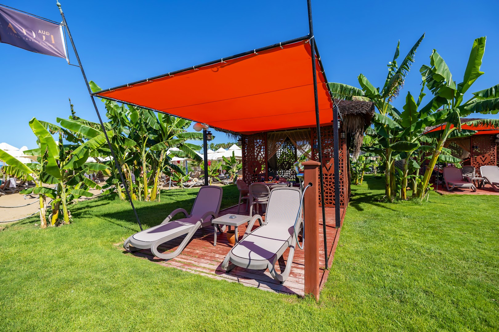 Vonresort Elite dārza atpūtas zona ar sauļošanās krēsliem, oranžu nojumi un palmām zālienā pie pludmales