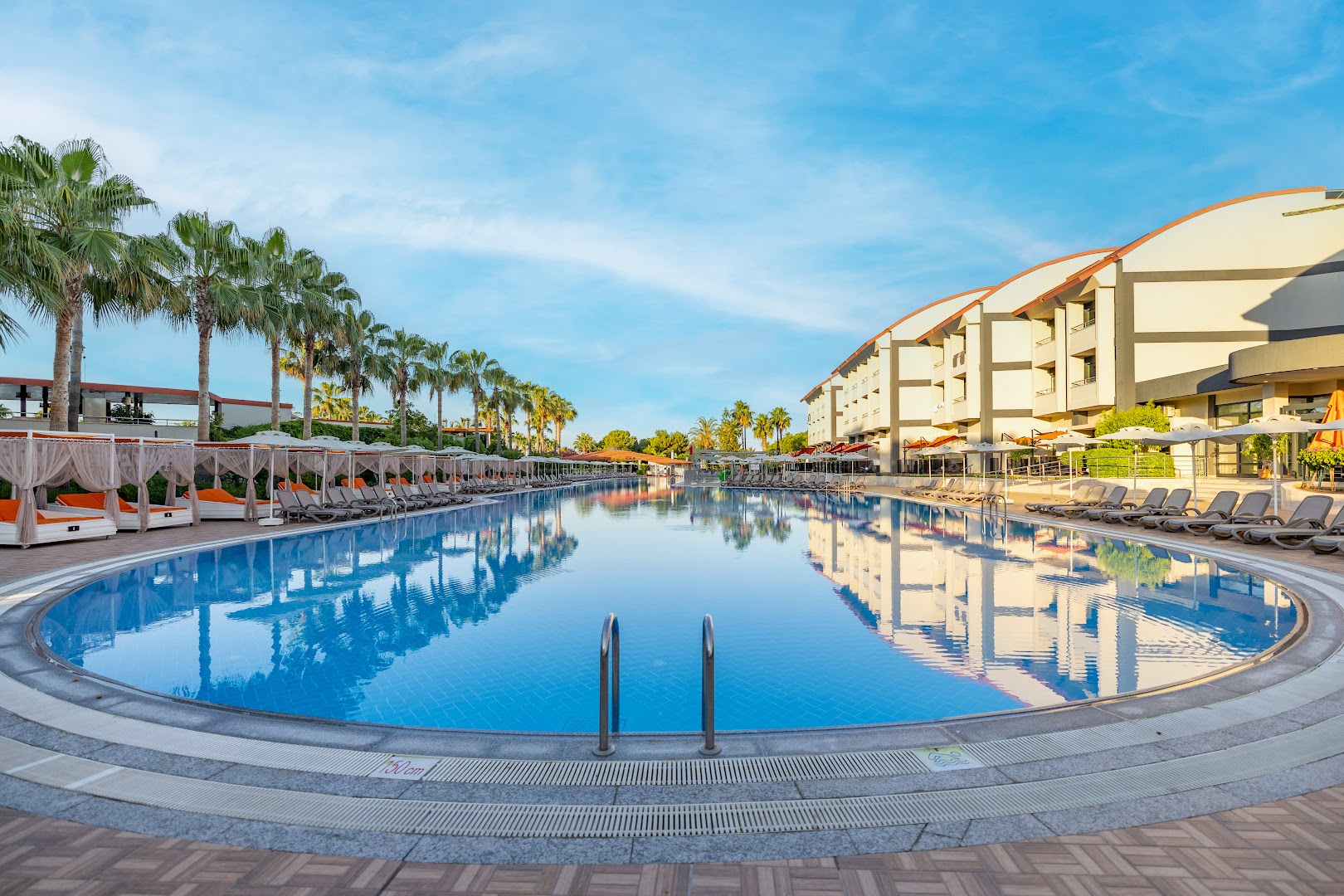 Vonresort Elite viesnīcas baseina zona ar saulessargiem, gultām un palmu aleju saulainā dienā Turcijā