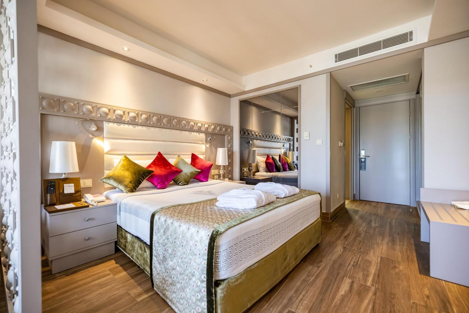 Vonresort Elite viesnīcas numurs ar divguļamo gultu, košiem dekoratīvajiem spilveniem un koka grīdu Side reģionā, Turcijā