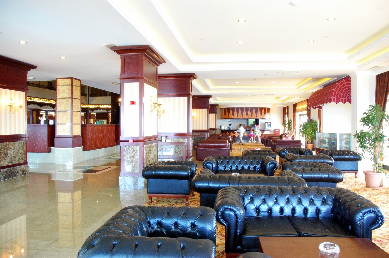 Utopia World Hotel plašais vestibils Alanjā ar tumšas ādas dīvāniem, klasisku koka apdari un lobby bāru fonā
