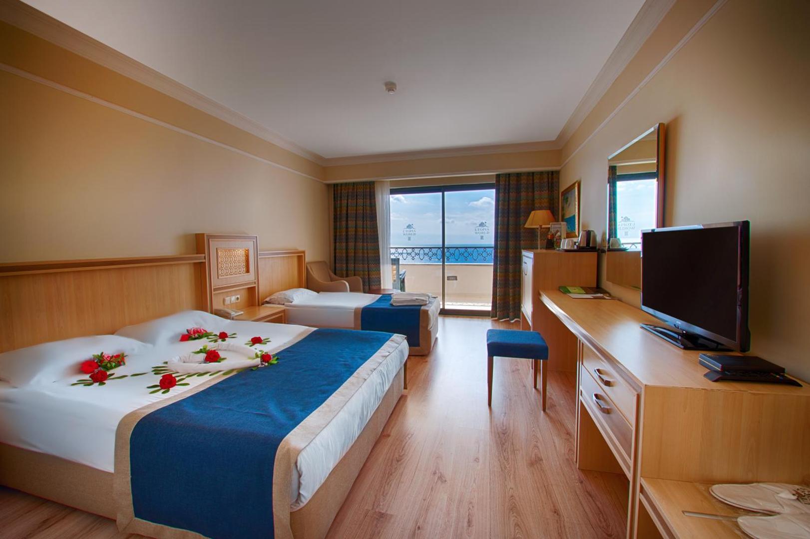Utopia World Hotel gaišs standarta numurs ar divām gultām, koka mēbelēm un balkonu ar skatu uz jūru Alānijā.