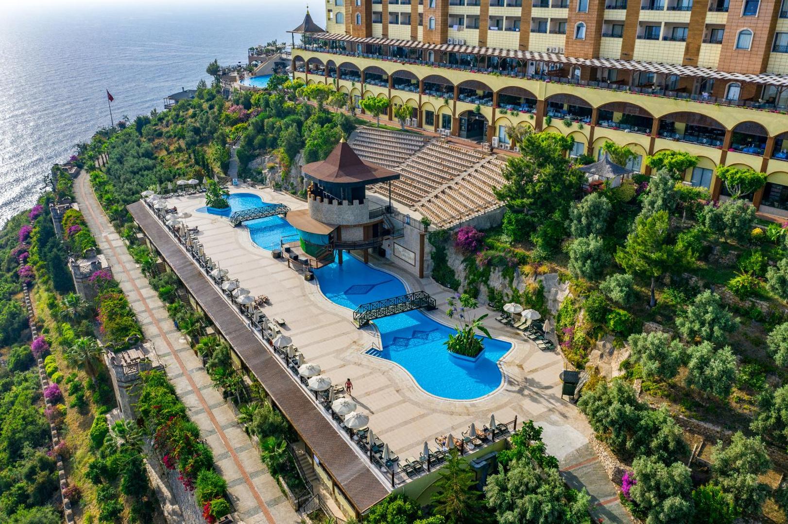 Utopia World Hotel āra baseinu zona ar tiltiņiem un amfiteātri kalna nogāzē ar skatu uz jūru Turcijā.