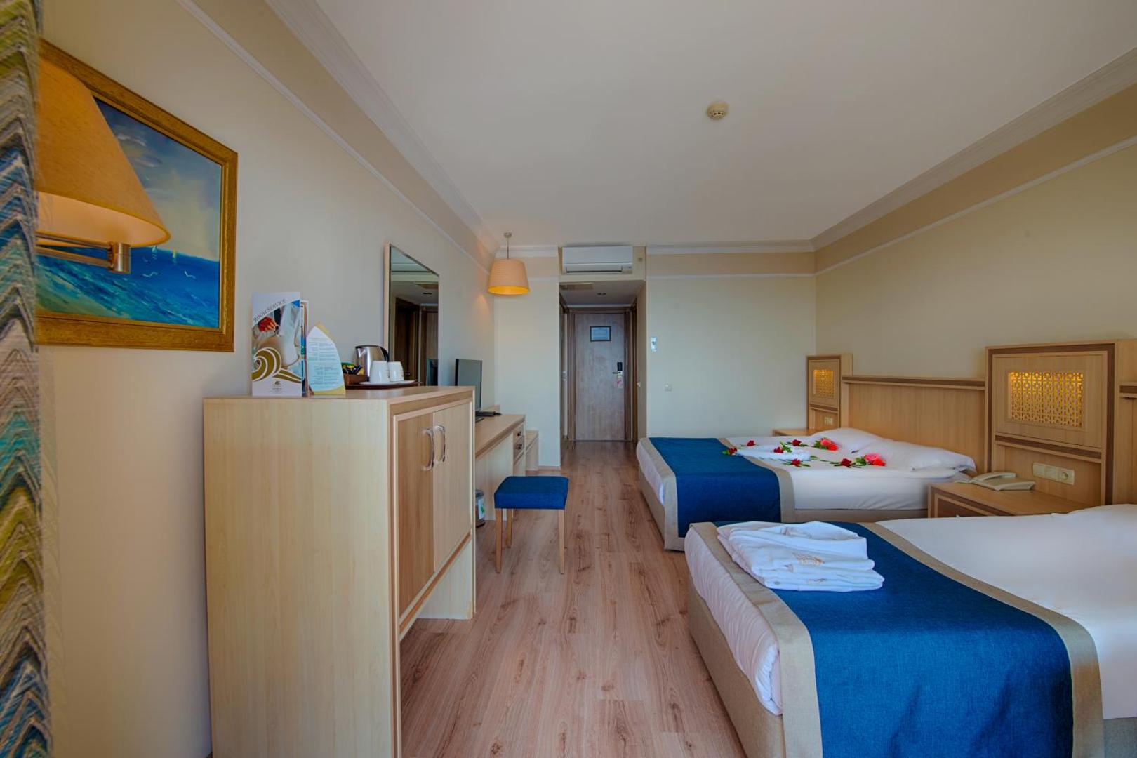 Utopia World Hotel numura interjers ar divām gultām, lamināta grīdu un skatu uz ieeju, Alānijas reģions.