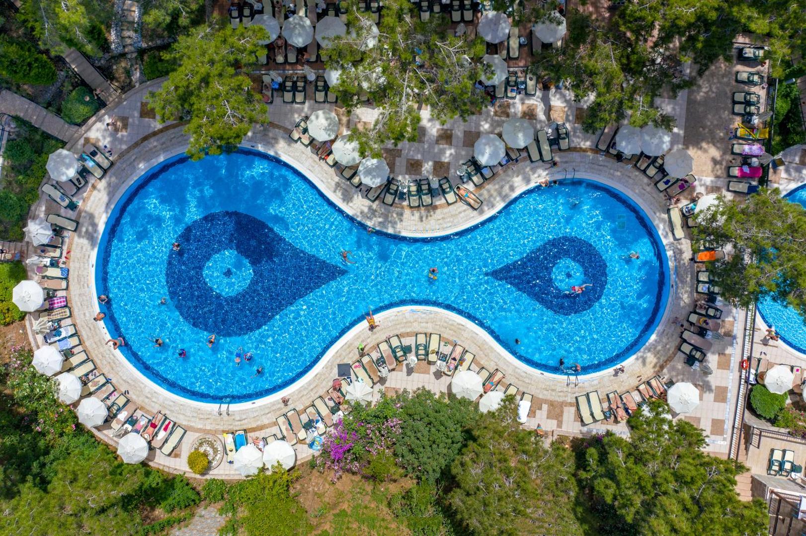 Utopia World Hotel skats no augšas uz zilo āra baseinu neparastā formā, ko ieskauj priežu mežs un sauļošanās krēsli Alanjā.