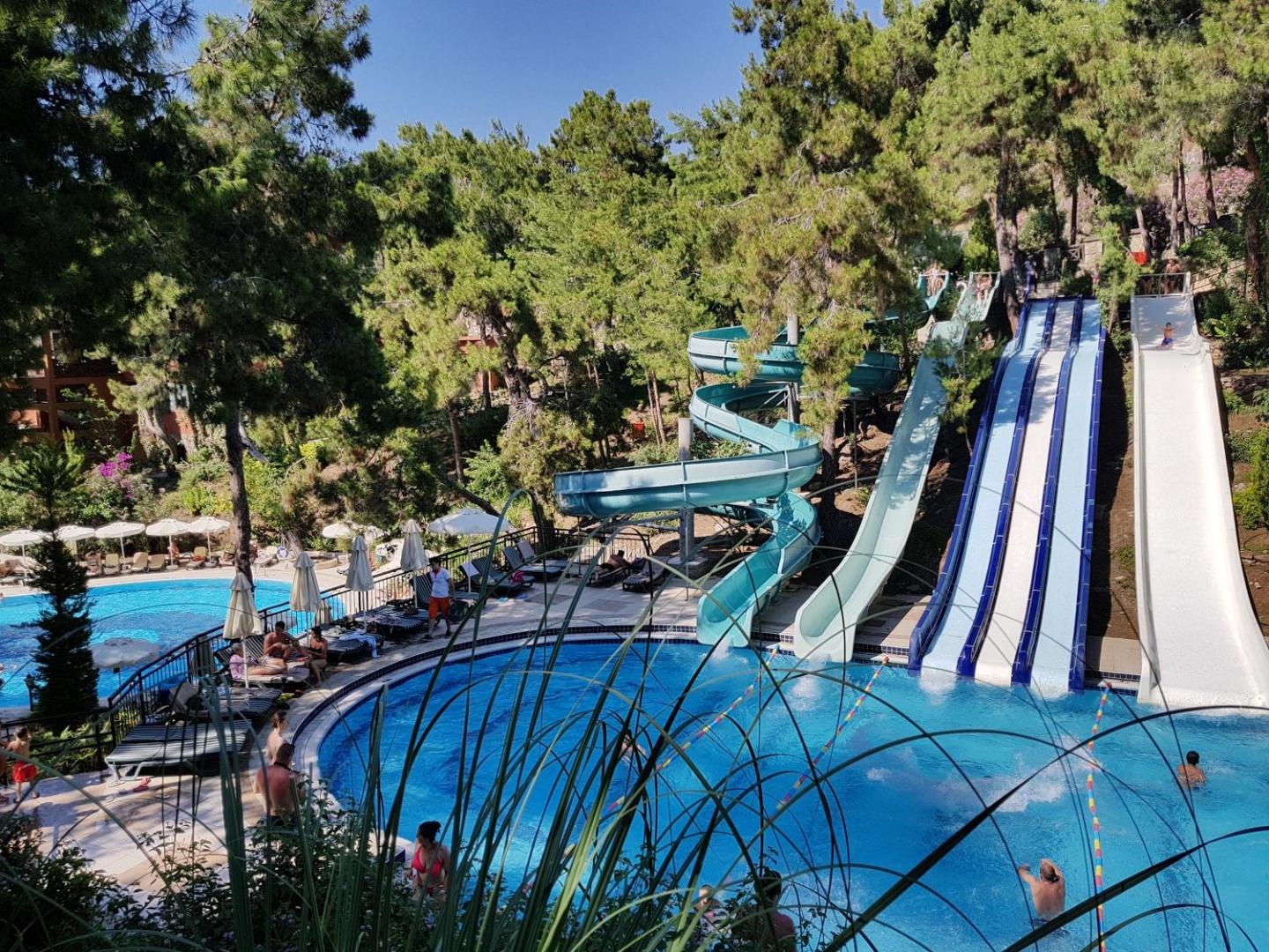 Utopia World Hotel akvaparks ar vairākiem krāsainiem ūdens slidkalniņiem un baseinu, ko ieskauj kupli zaļi koki Turcijas piekrastē.