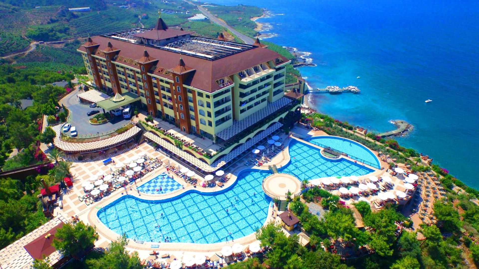Utopia World Hotel panorāmas skats uz galveno ēku, lielajiem baseiniem un Vidusjūras piekrasti no putna lidojuma Alanjā.