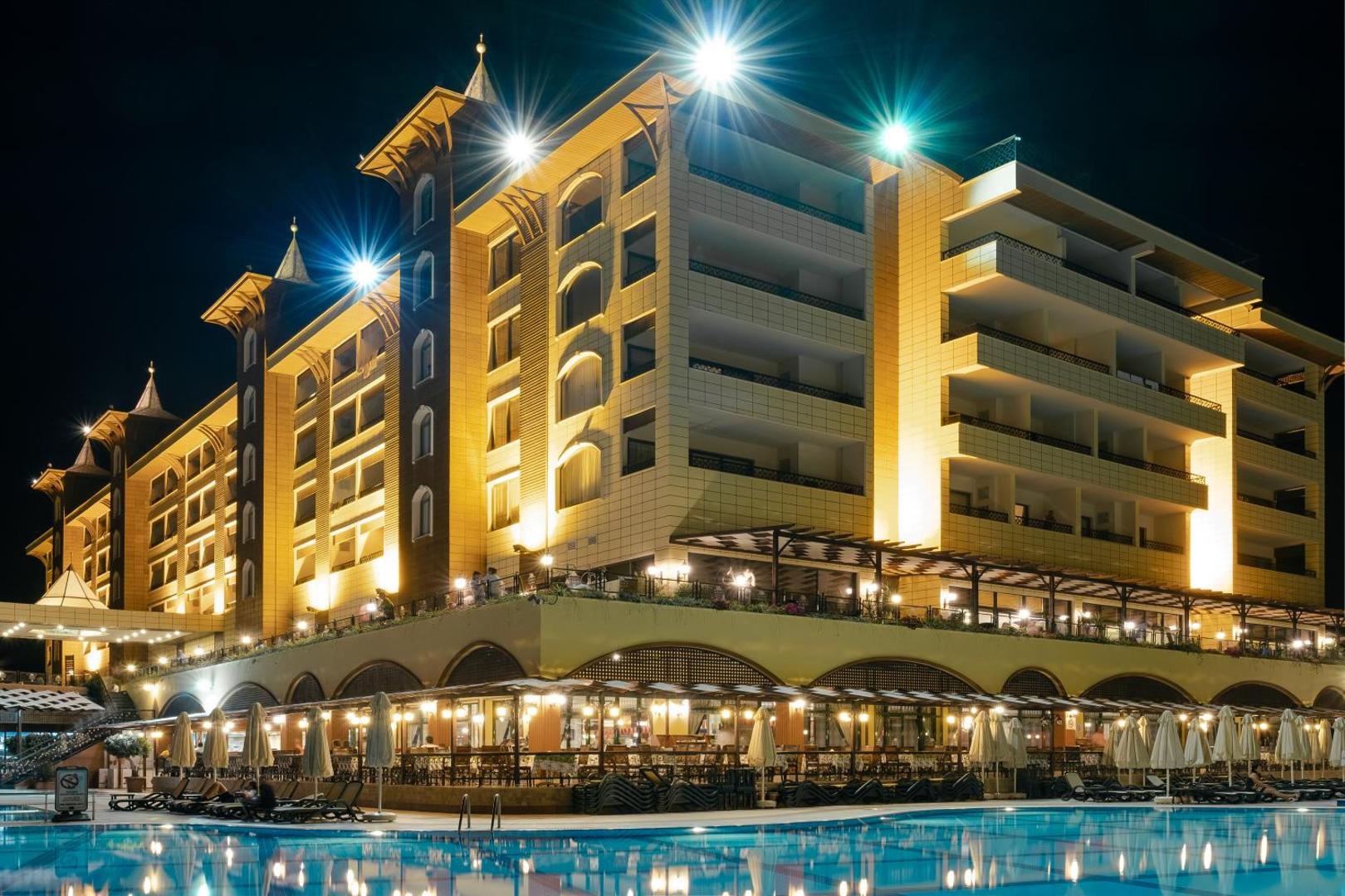 Utopia World Hotel galvenā ēka naktī pie baseina — izgaismoti numuri, restorāna terase un vakara atmosfēra
