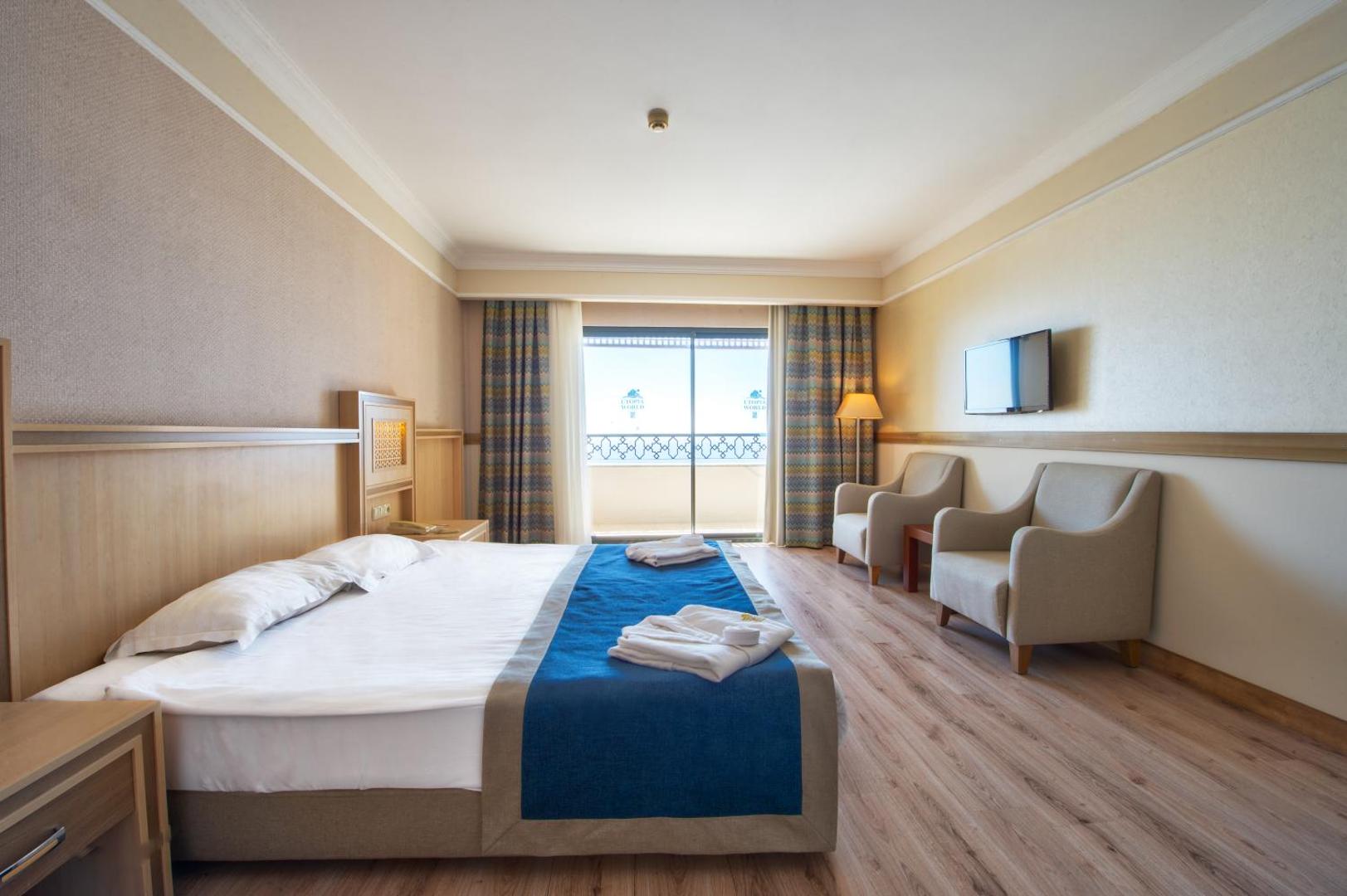 Utopia World Hotel numurs ar divguļamo gultu, atpūtas zonu ar krēsliem un plašu logu uz jūru Alānijā.
