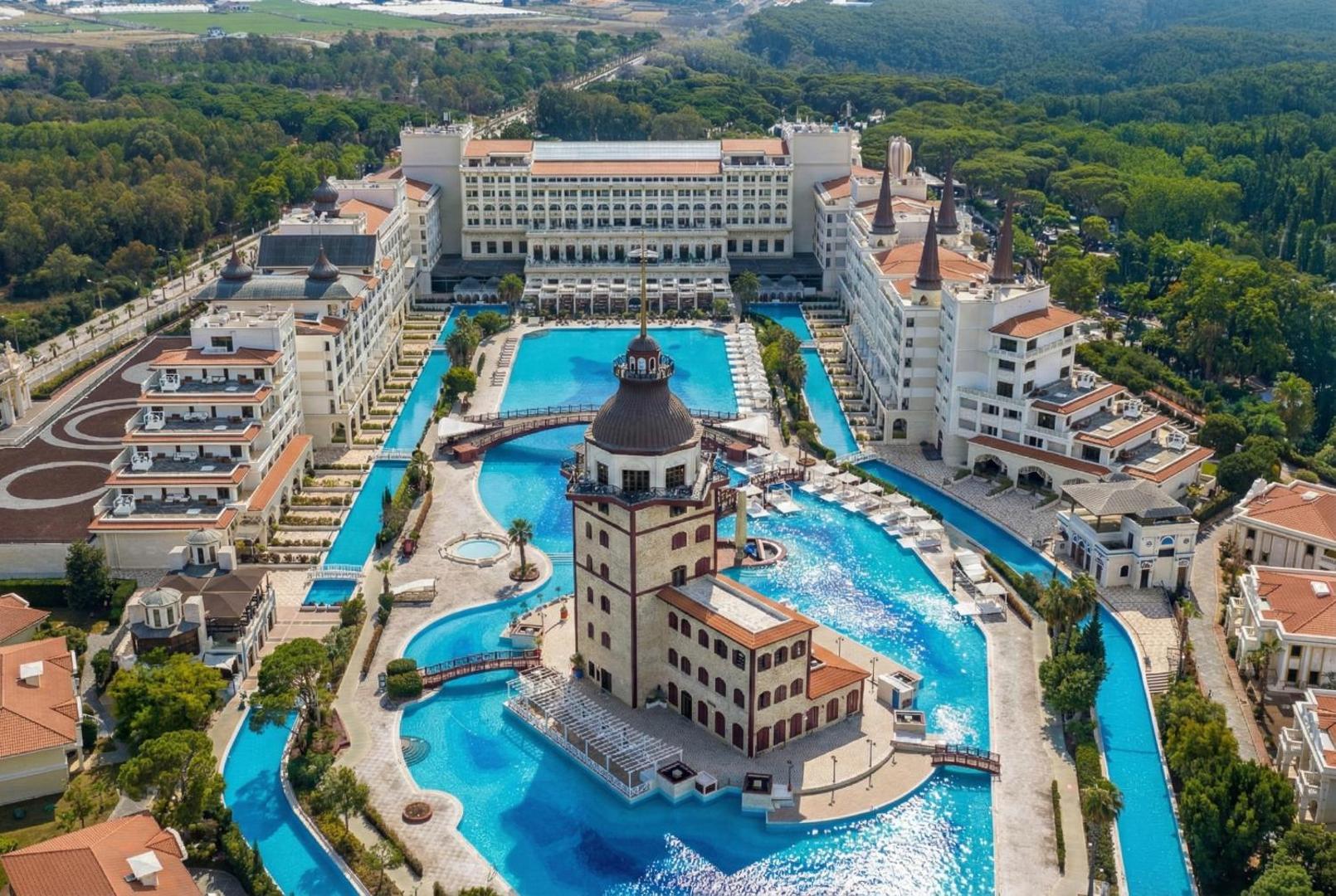 Titanic Mardan Palace viesnīcas panorāmas skats no augšas Antālijā — plašs baseinu komplekss ar centrālo torni un greznu arhitektūru