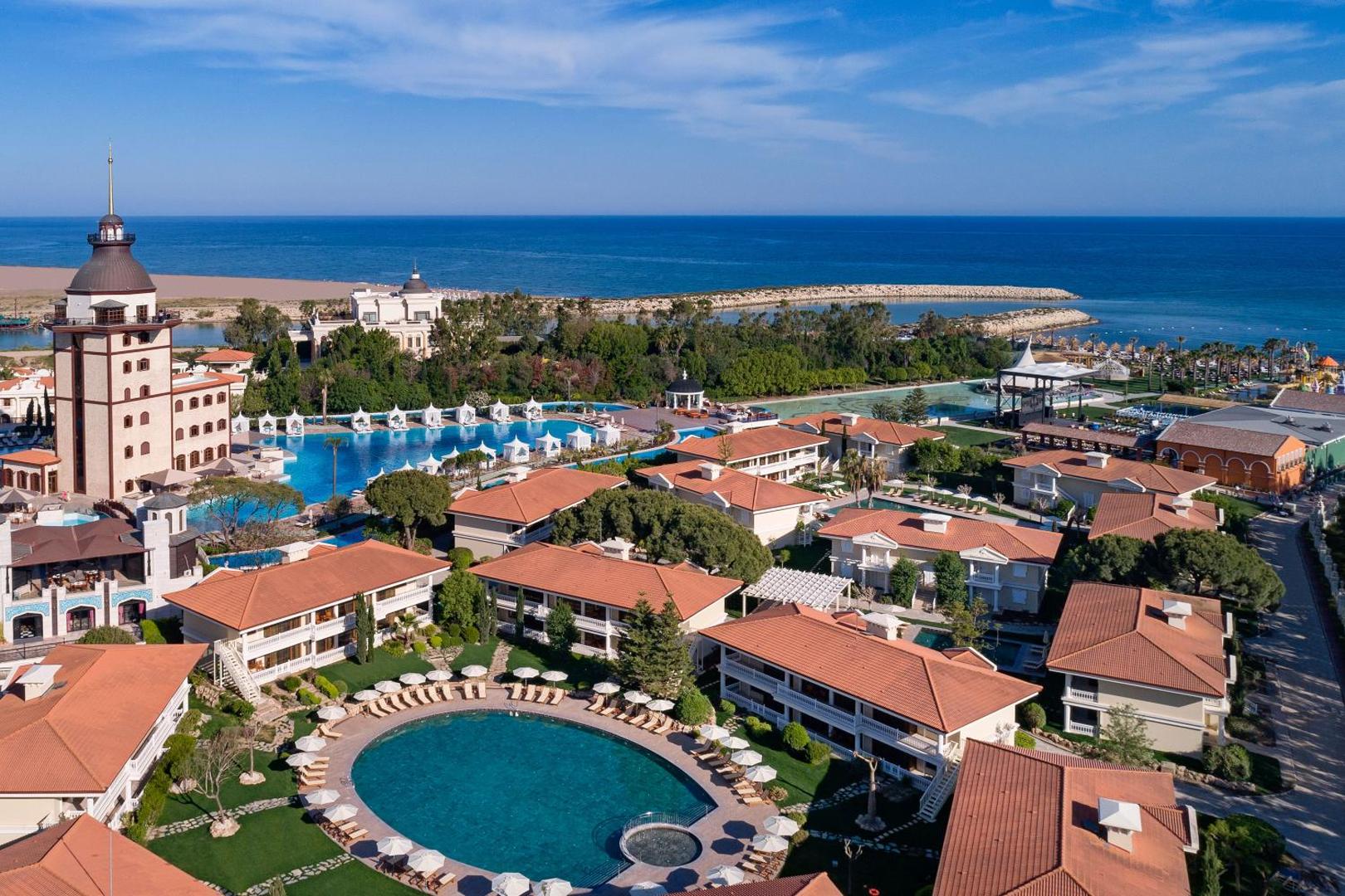 Skats uz Titanic Mardan Palace bungalo tipa numuriem un dārza baseinu piekrastē ar jūru fonā Turcijā