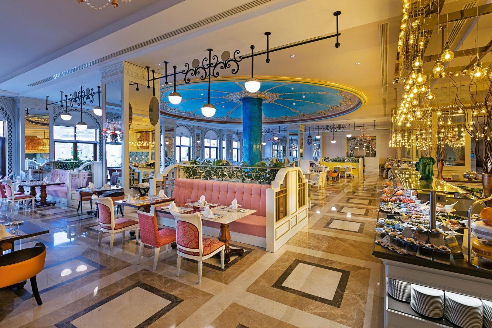 Titanic Mardan Palace viesnīcas restorāns ar greznu interjeru, rozā dīvāniem, dekoratīviem griestiem un bagātīgu bufetes zonu.